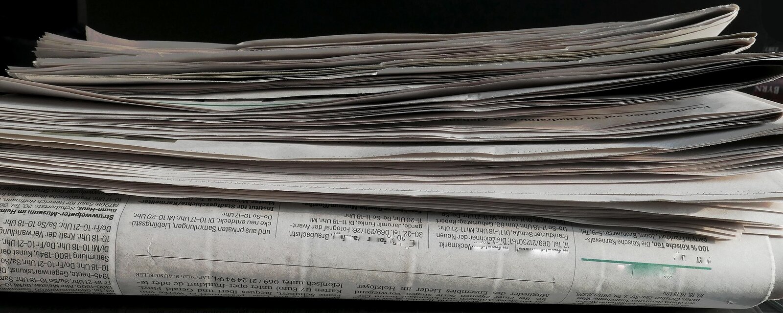 Ein Stapel mehrfach gefalteter Zeitungen liegt auf einer glatten Oberfläche. Die schwarz-weiße Aufnahme betont die Struktur und Faltung des Papiers.