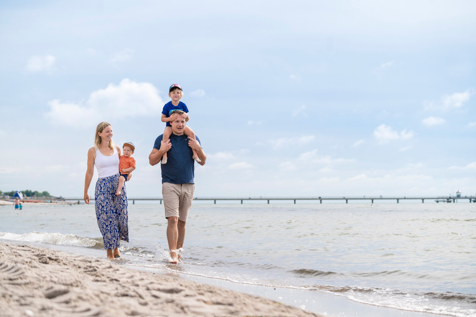 Eine Familie spaziert am Strand entlang. Es ist Sommer.