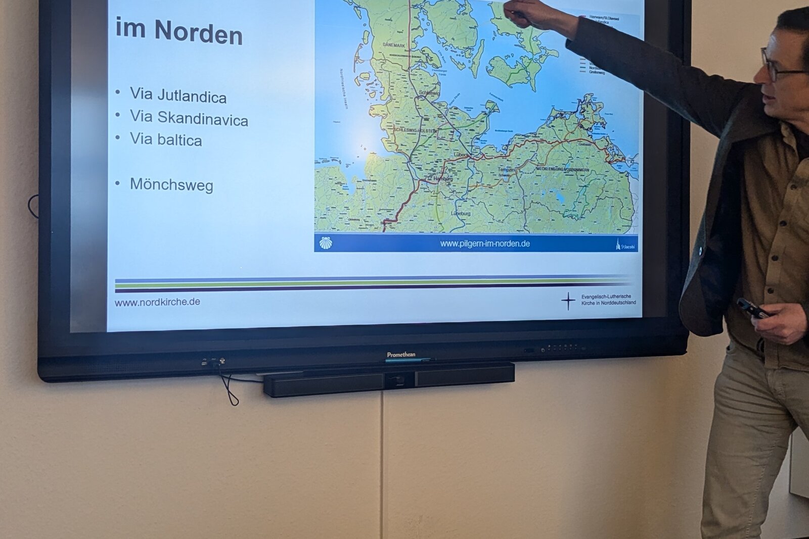 Eine Person steht vor einem digitalen Bildschirm und erläutert eine Abbildung zum Thema Pilgern im Norden. 
