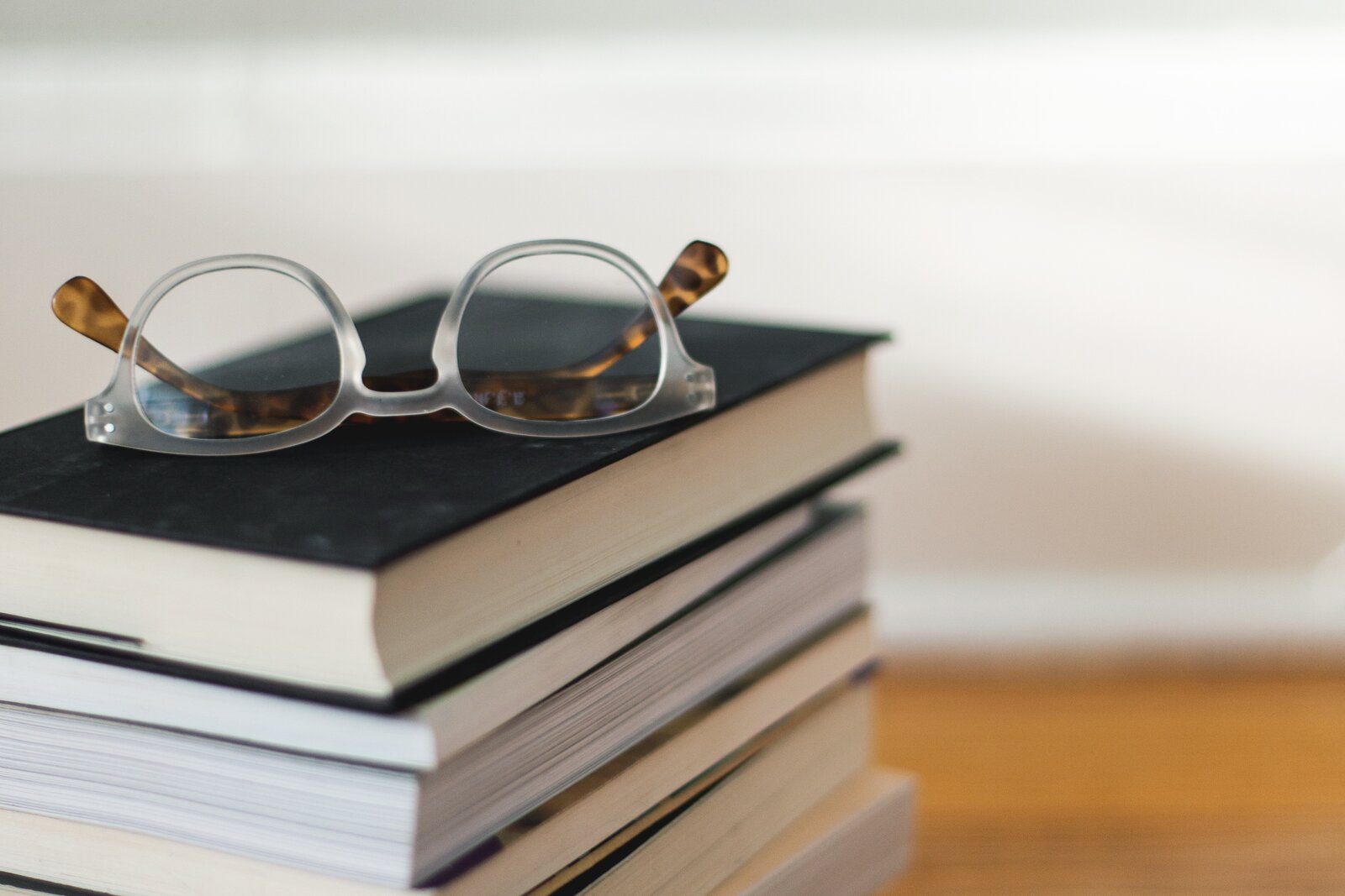 Das Bild zeigt einen Stapel B&uuml;cher, von dem man sie Seiten sieht und auf dem eine Brille platziert ist.