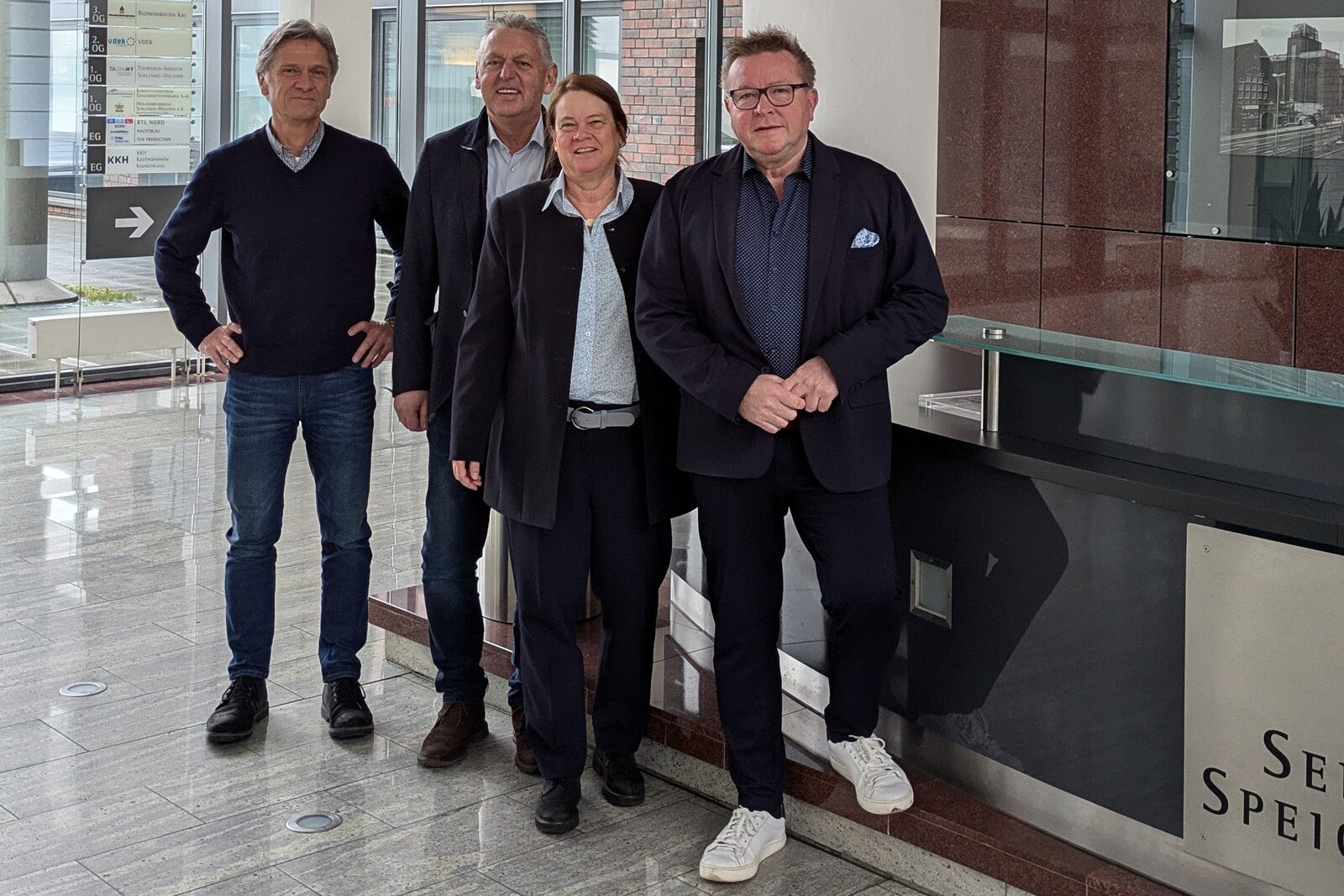 Auf dem Bild sind von links nach rechts Peter Douven, Manfred Wohnrade, Dr. Catrin Homp und Hans-Jürgen Lütje in einem Foyer zu sehen.