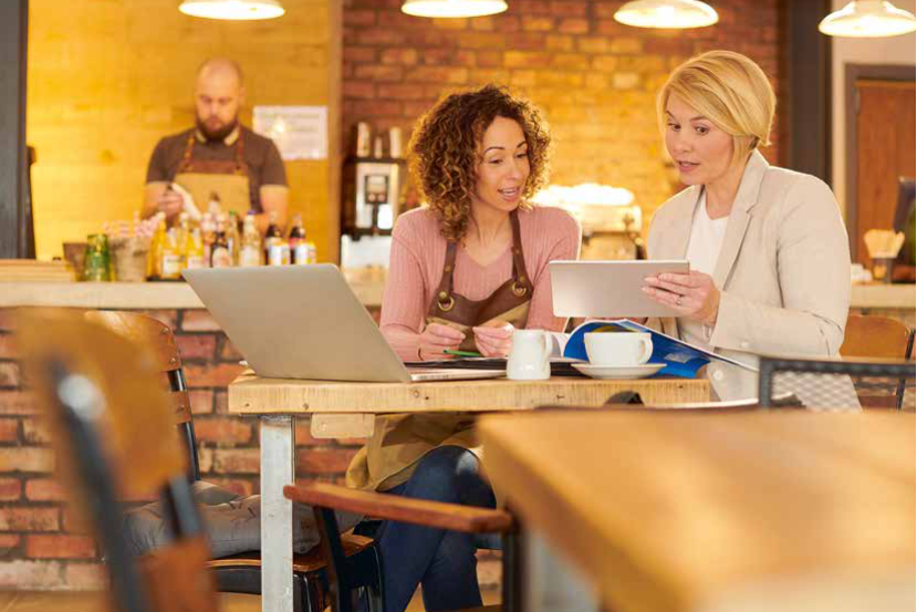 Zwei Frauen unterhalten sich in einem Café über ein Tablet.