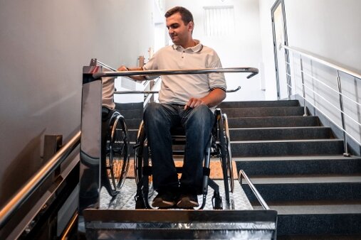 Ein Mann sitzt in einem Rollstuhl und nutzt einen Treppenlift, um sicher eine Treppe in einem modernen Gebäude zu überwinden.